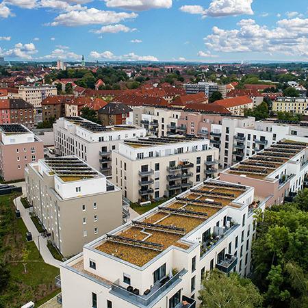 Drohnenansicht aller Gebaeude des Wohnquatiers in Braunschweig mit heller Fassade, Dachterrassen, Terassen, Gaerten, Solarpanelen und Balkonen