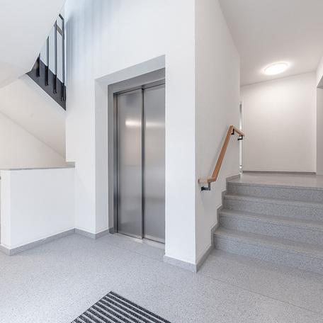 Treppenaufgang und Aufzug des Wohn- und Gewerbequatiers York in Muenster mit weissen Waenden und graumiliertem Boden