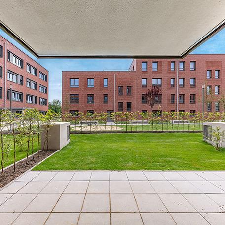 Blick frontal auf eine Gebaeudereihe des Wohnquatier York in Muenster aus der Sicht einer Terrasse mit Garten